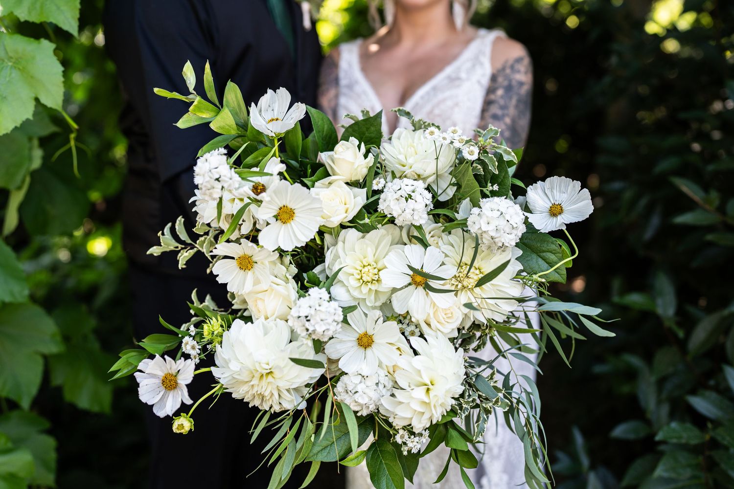 Elegant white and green wedding bouquet with daisies and mixed florals in natural sunlight.