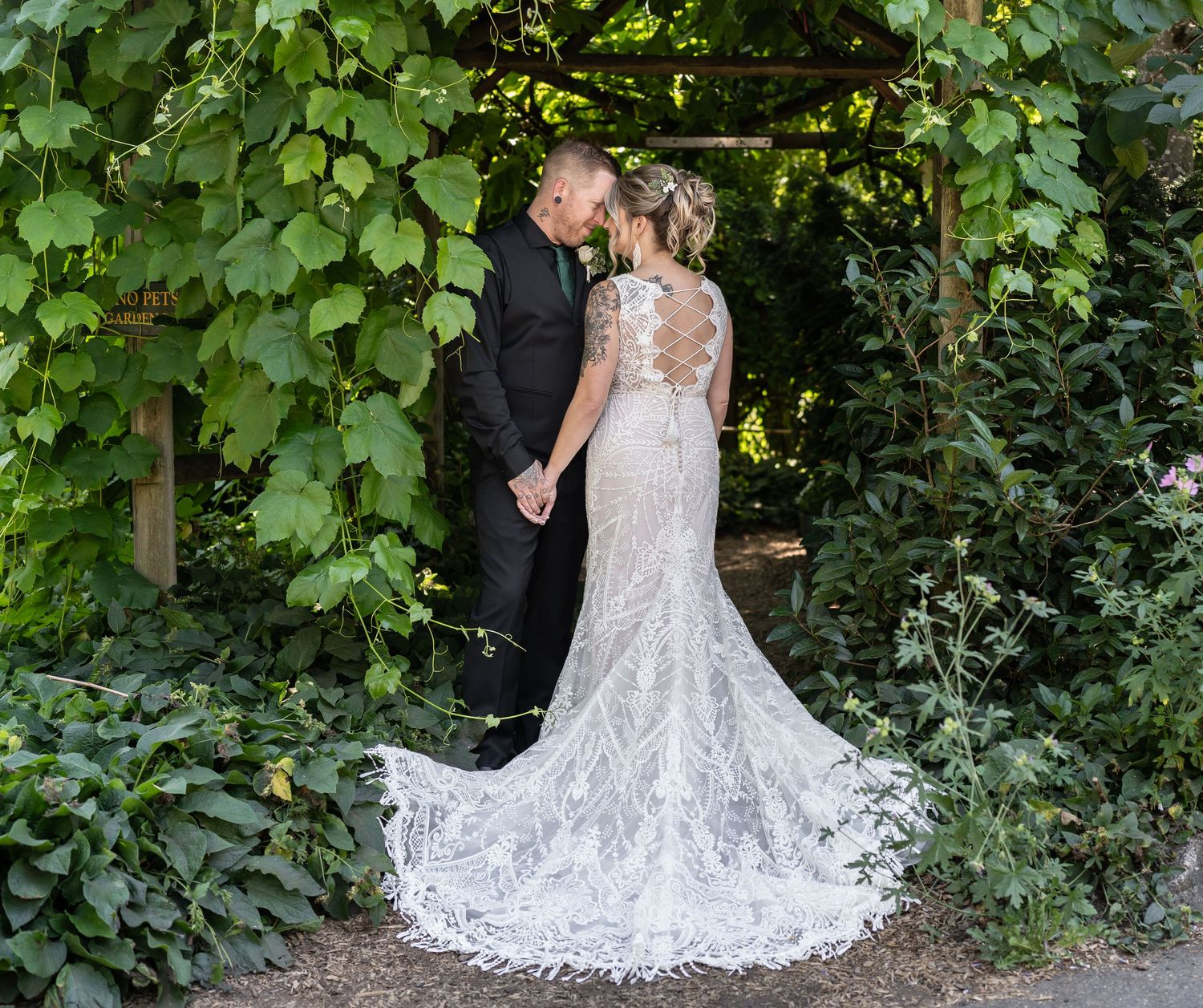 A stunning lace wedding dress with long train photographed in a romantic garden archway covered in greenery.