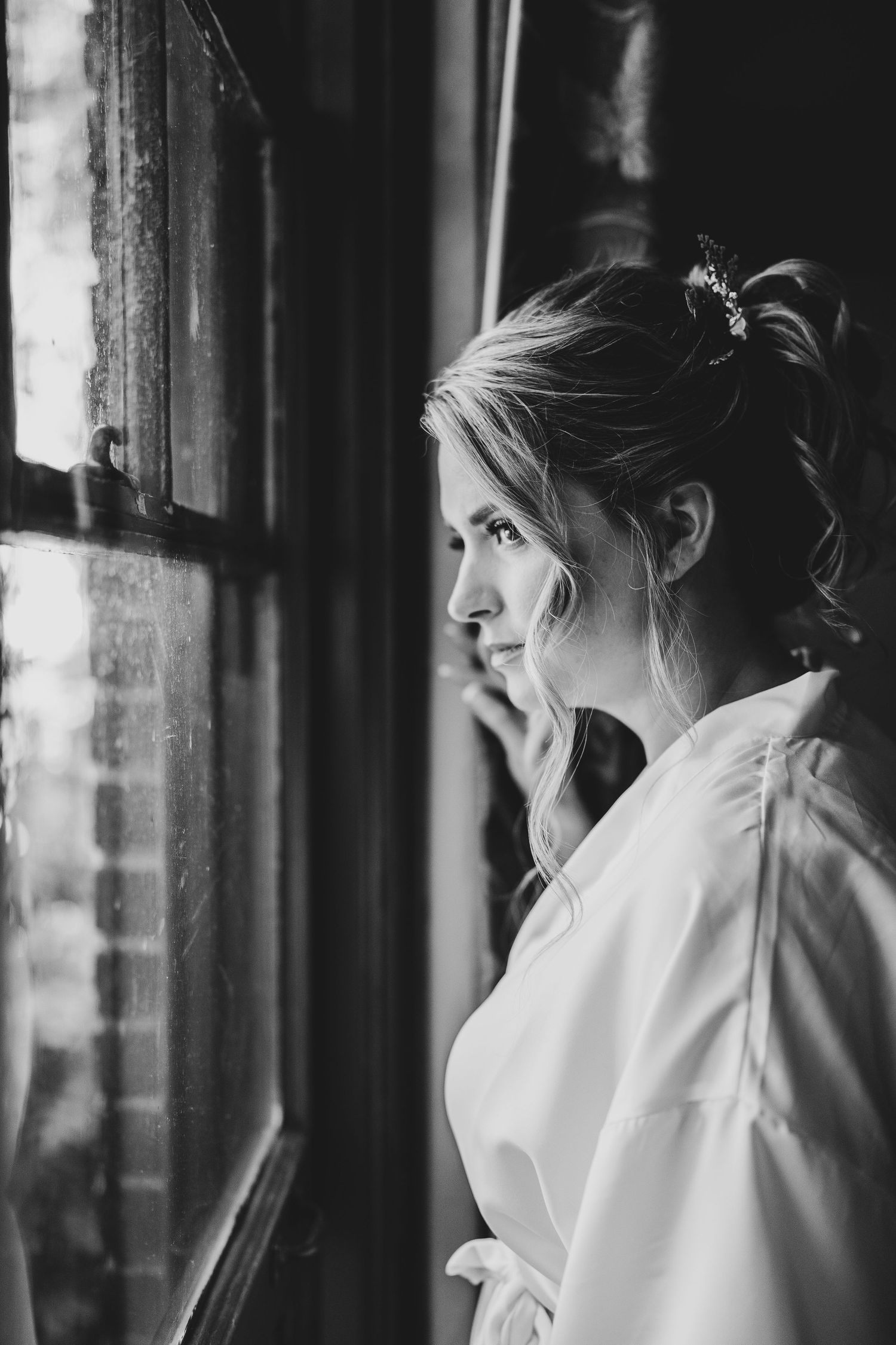 Artistic black and white portrait of woman in white robe gazing out window.