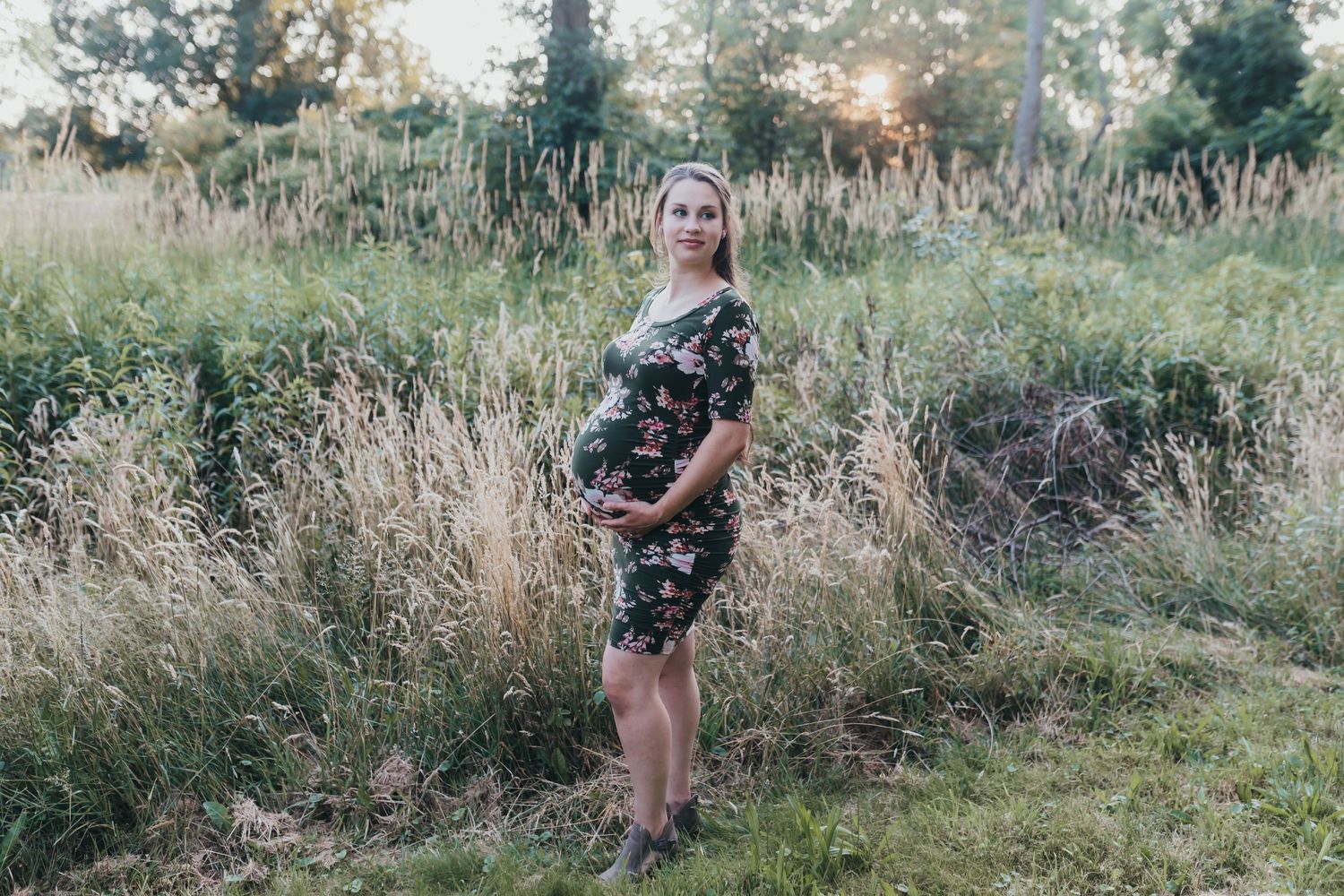 Pregnant woman stands for her maternity photo session near Fredericksburg PA in long grasses at golden hour.
