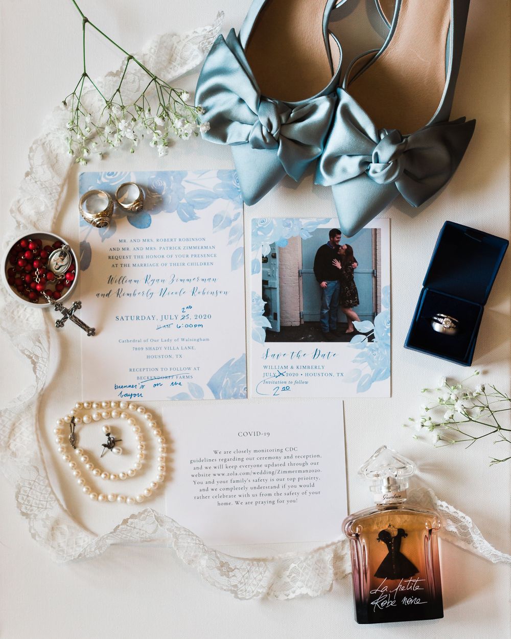 Wedding flatlay with blue shoes, invitations, perfume, pearls and baby's breath flowers.