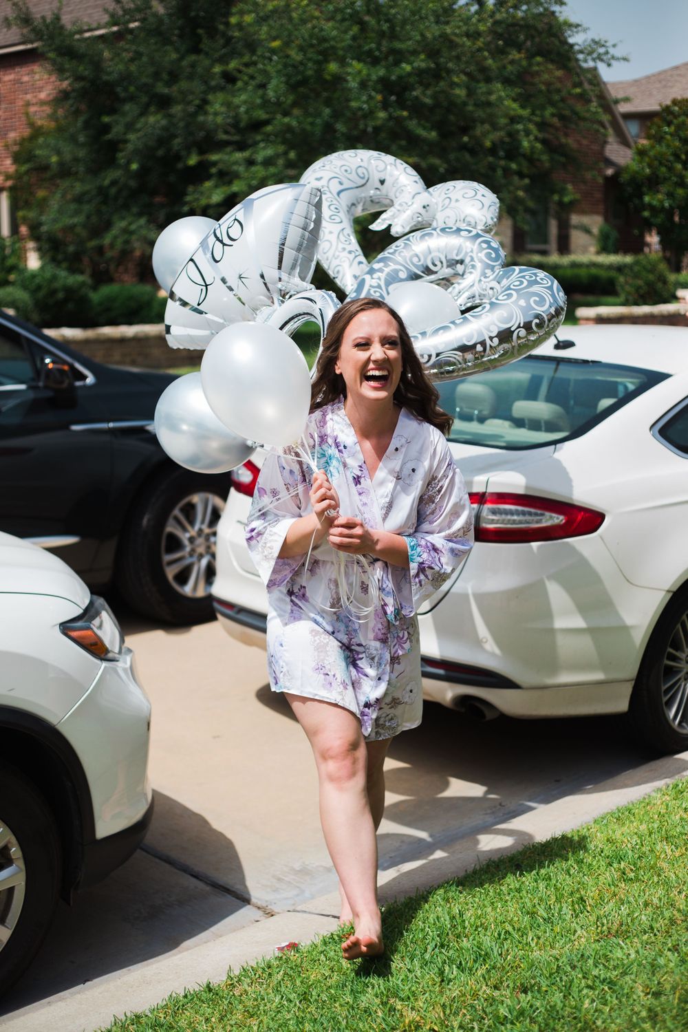 Person holding silver and white balloons while standing between parked cars on a sunny day.