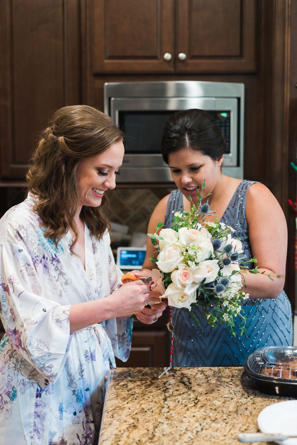 Two people examining a floral bouquet with white flowers in a kitchen with dark cabinets.