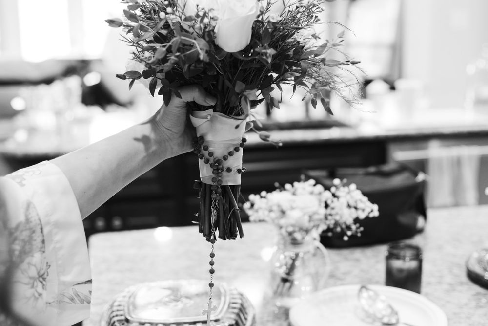 Black and white photo of hands arranging flowers in a vase on a table setting.