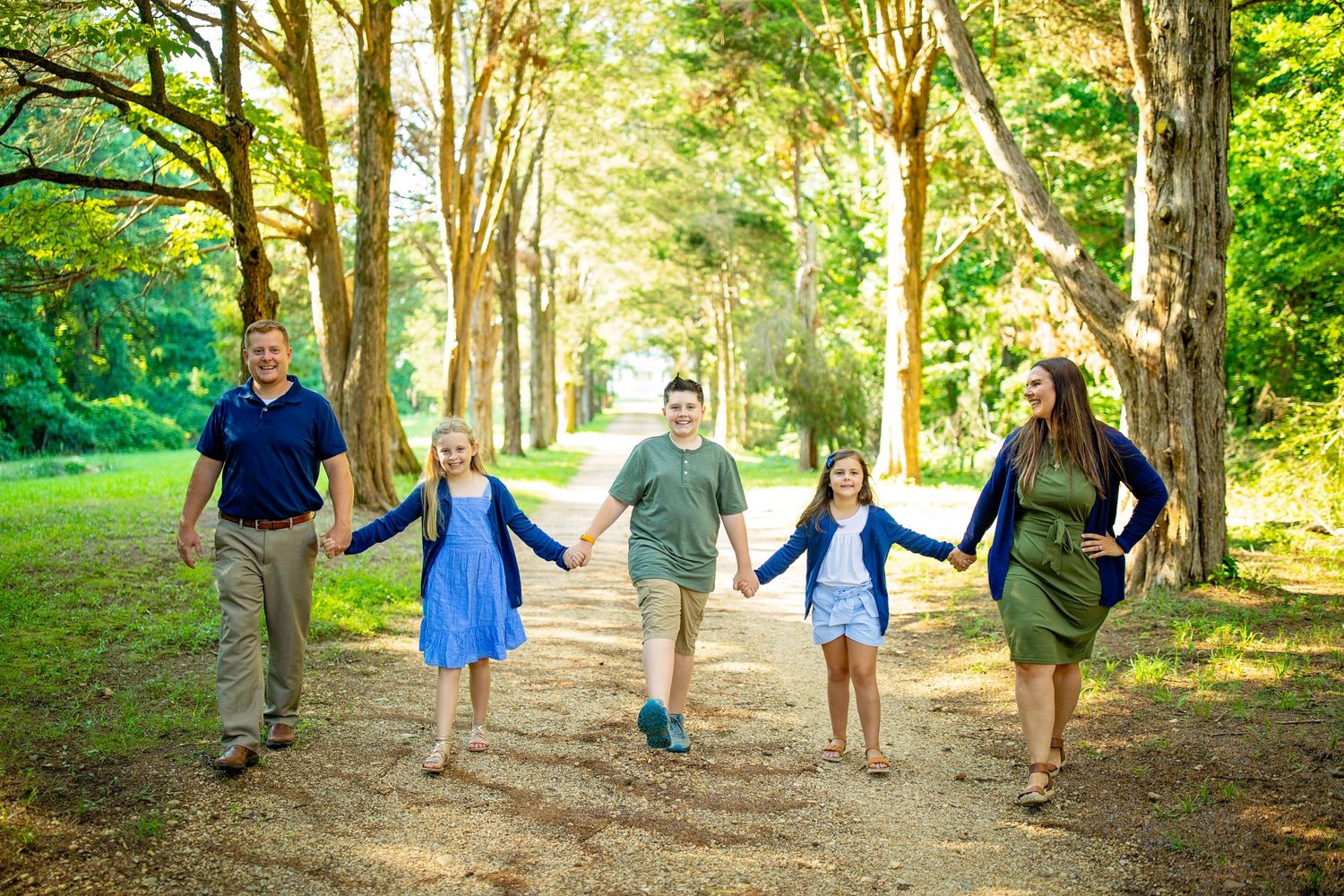 A group walking together and holding hands along a tree-lined path on a sunny summer day.