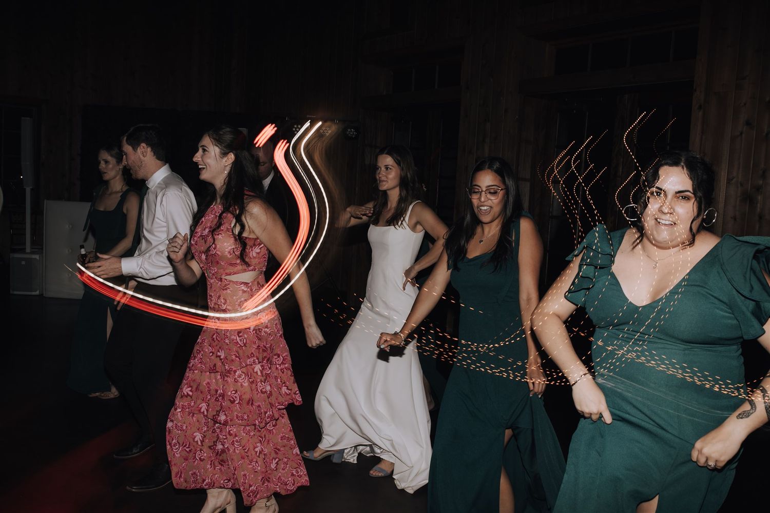 Group of wedding guests dancing with light-up props at a nighttime reception.
