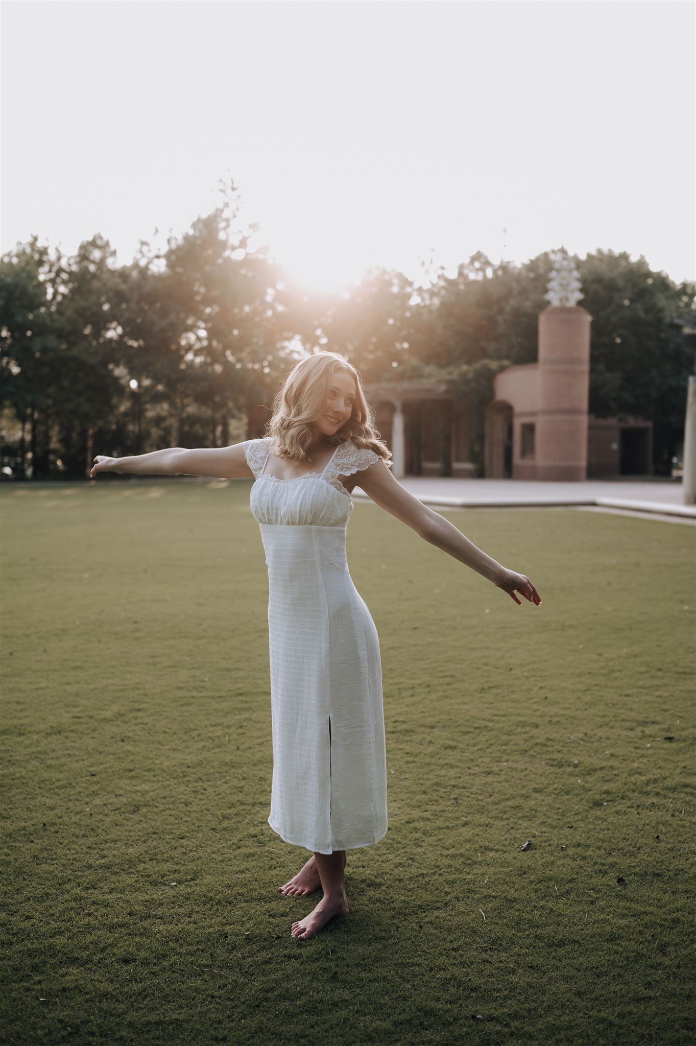 Joyful dance pose in white sundress during golden hour outdoors.