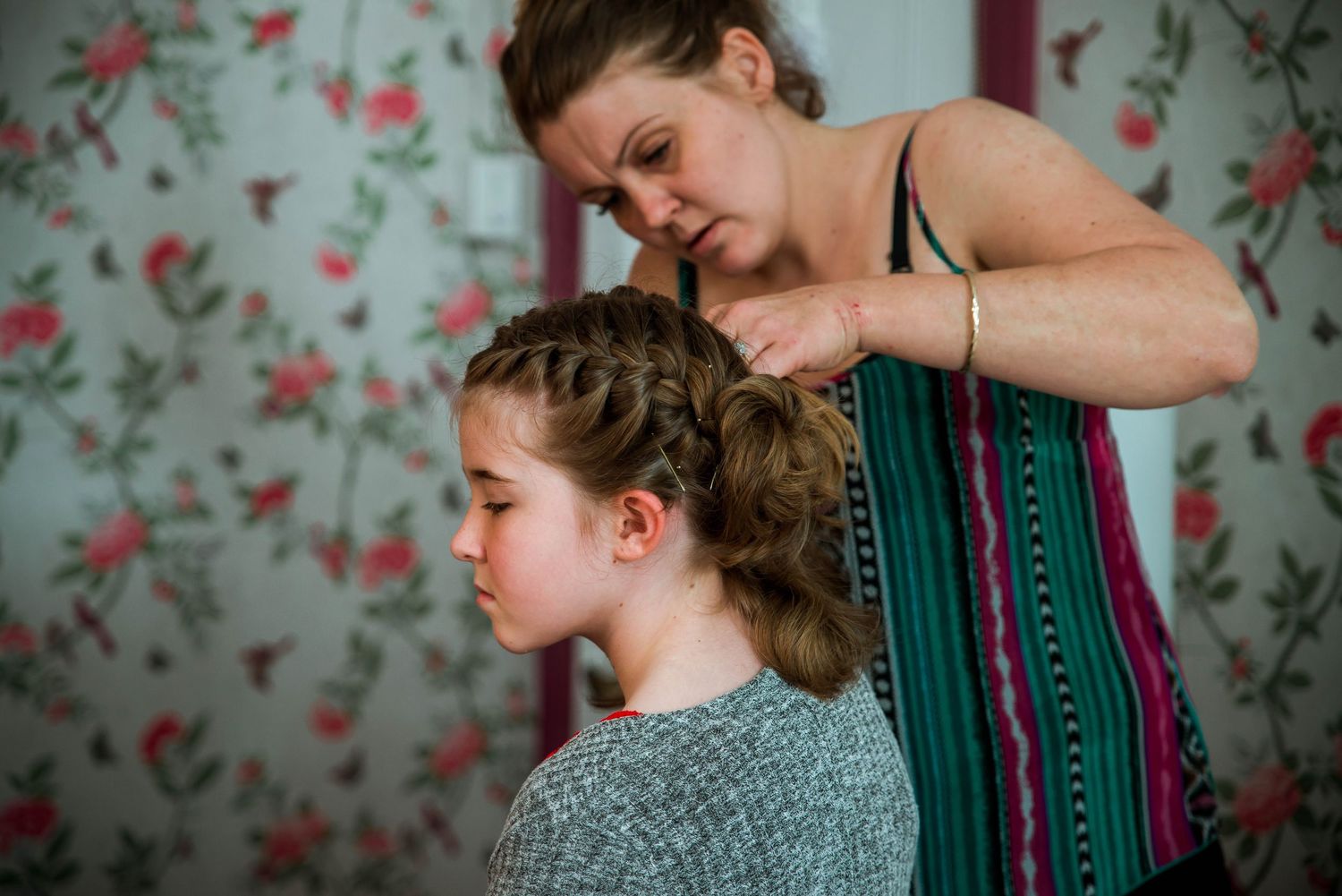 A touching moment captured against floral wallpaper as hair is styled with care.