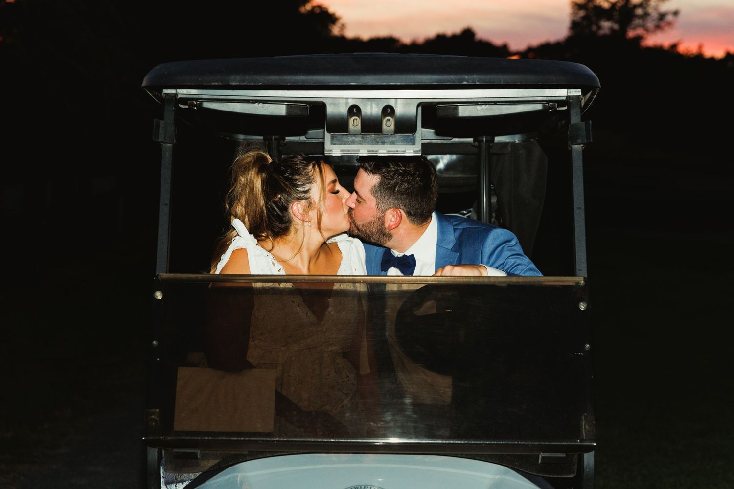 A couple shares a romantic moment in a golf cart at sunset on a golf course.