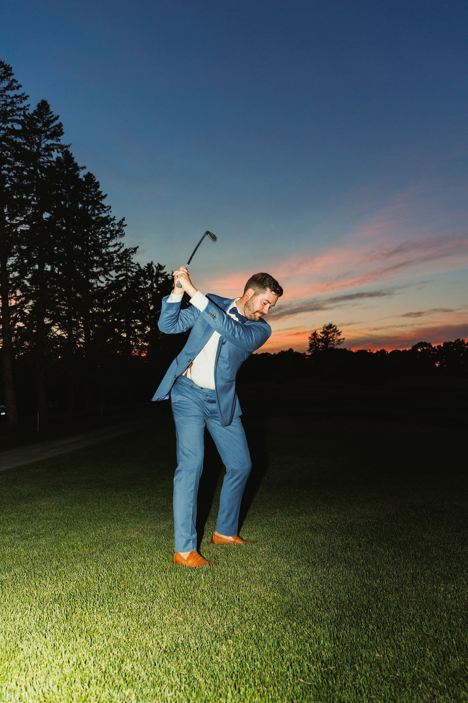 A person in blue dances on an illuminated grassy field at dusk.
