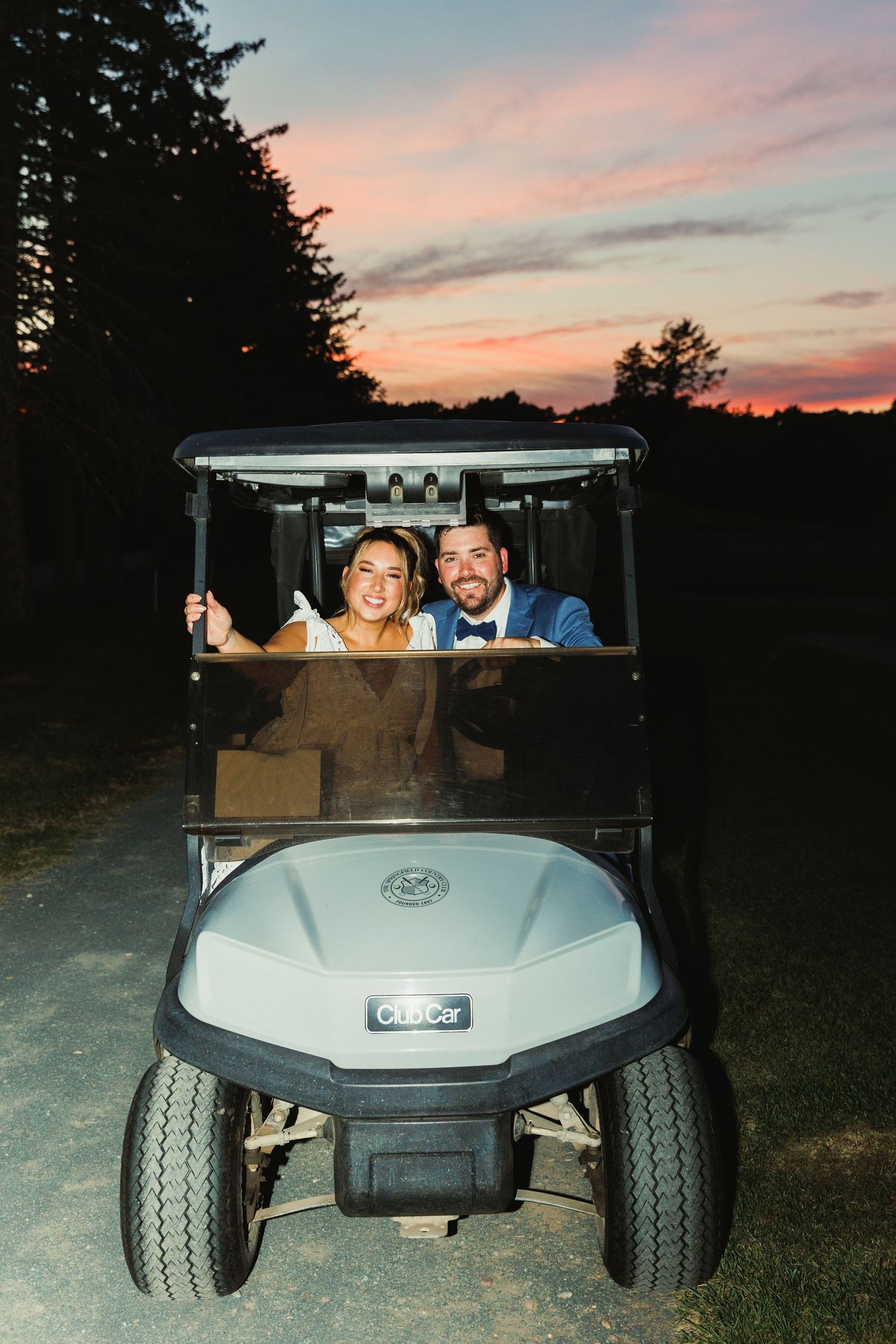 Golf cart parked on grass during a scenic sunset with pink and orange sky.