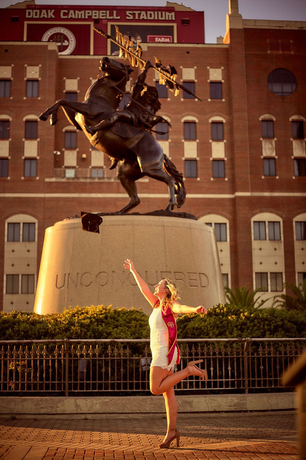 A woman standing in front of UNF's "Unconquered" statue during golden hour.