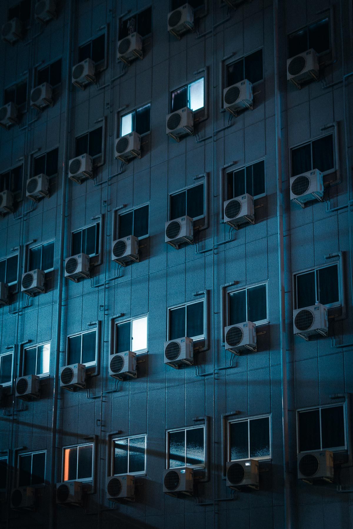 Modern building facade covered in air conditioning units glowing with cool blue light at night.