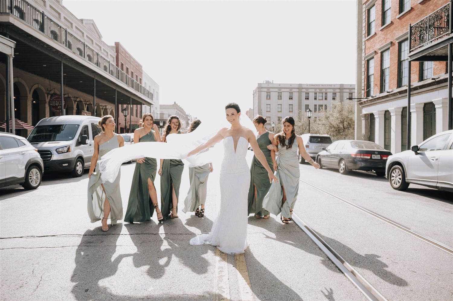 Bride and bridesmaids in sage dresses dancing on city street.