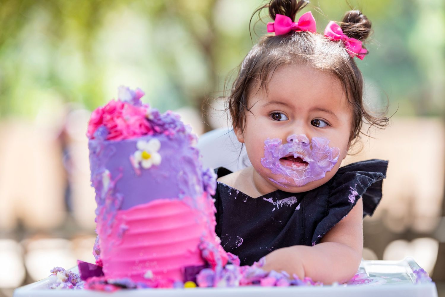 Orange County photographer captures Adorable toddler girl with cake smash birthday portrait covered in purple frosting outdoors.