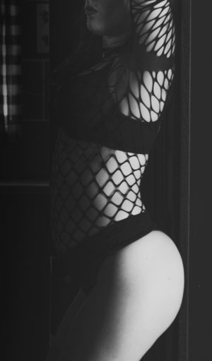 A woman in black fishnet lingerie poses standing for the best boudoir photographer in the Phoenix Arizona area