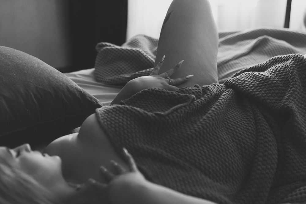 A woman nude covered in a blanket in bed poses for the best boudoir photographer in the Phoenix Arizona area