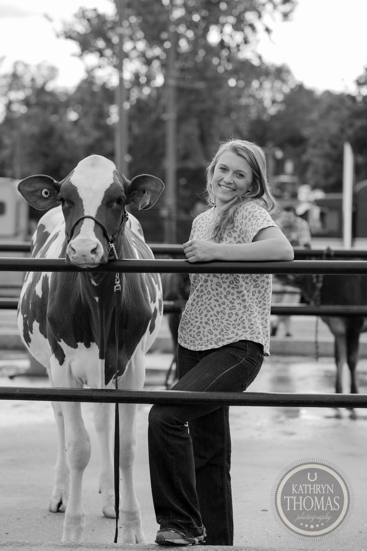 A black and white photo shows a dairy cow and person posing together at a rural event.