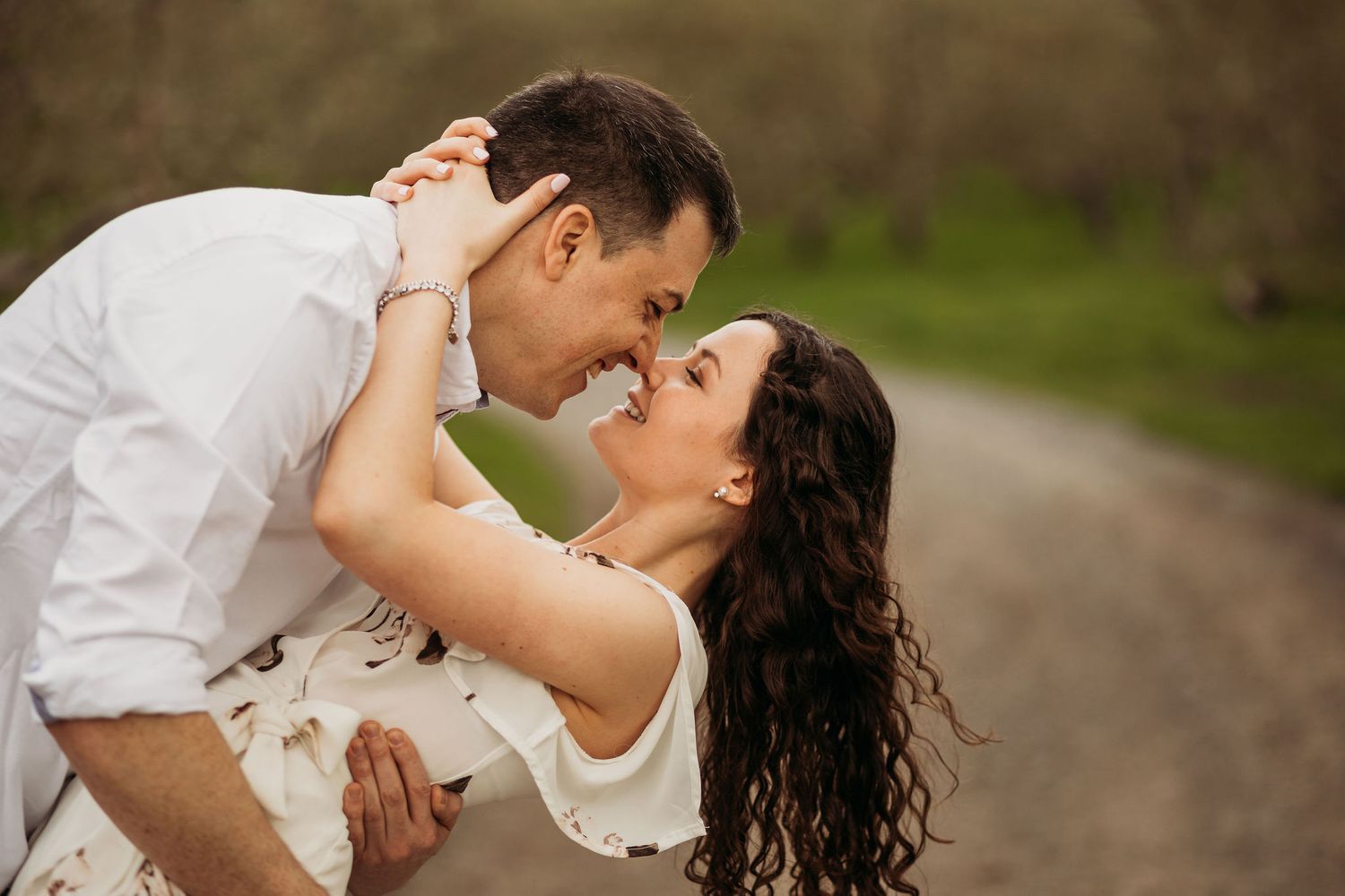 A romantic dip pose captured in warm lighting with spring foliage in the background.