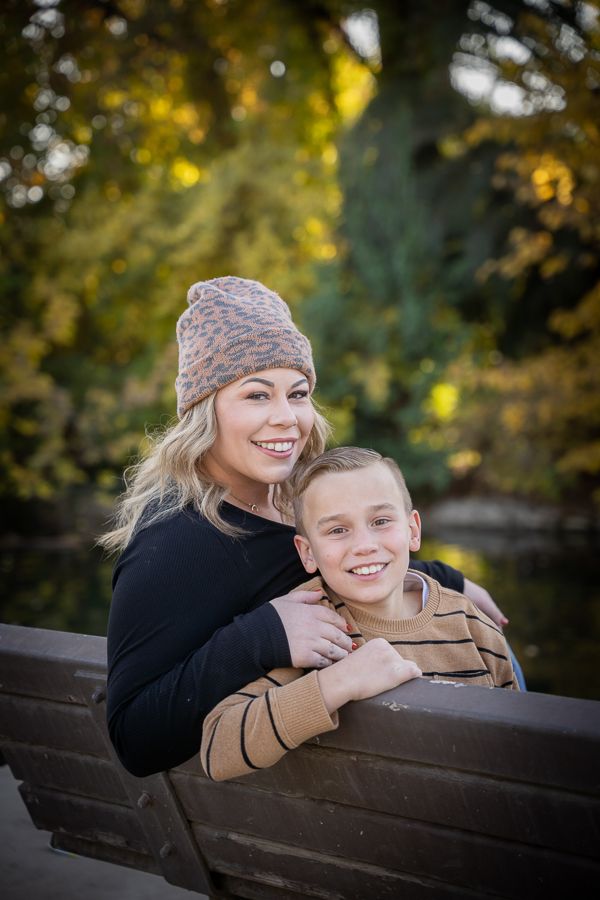 Autumn portrait session on wooden bench with fall foliage in background.