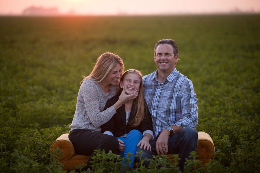 Family relaxing on blanket during sunset photo session in grassy field.