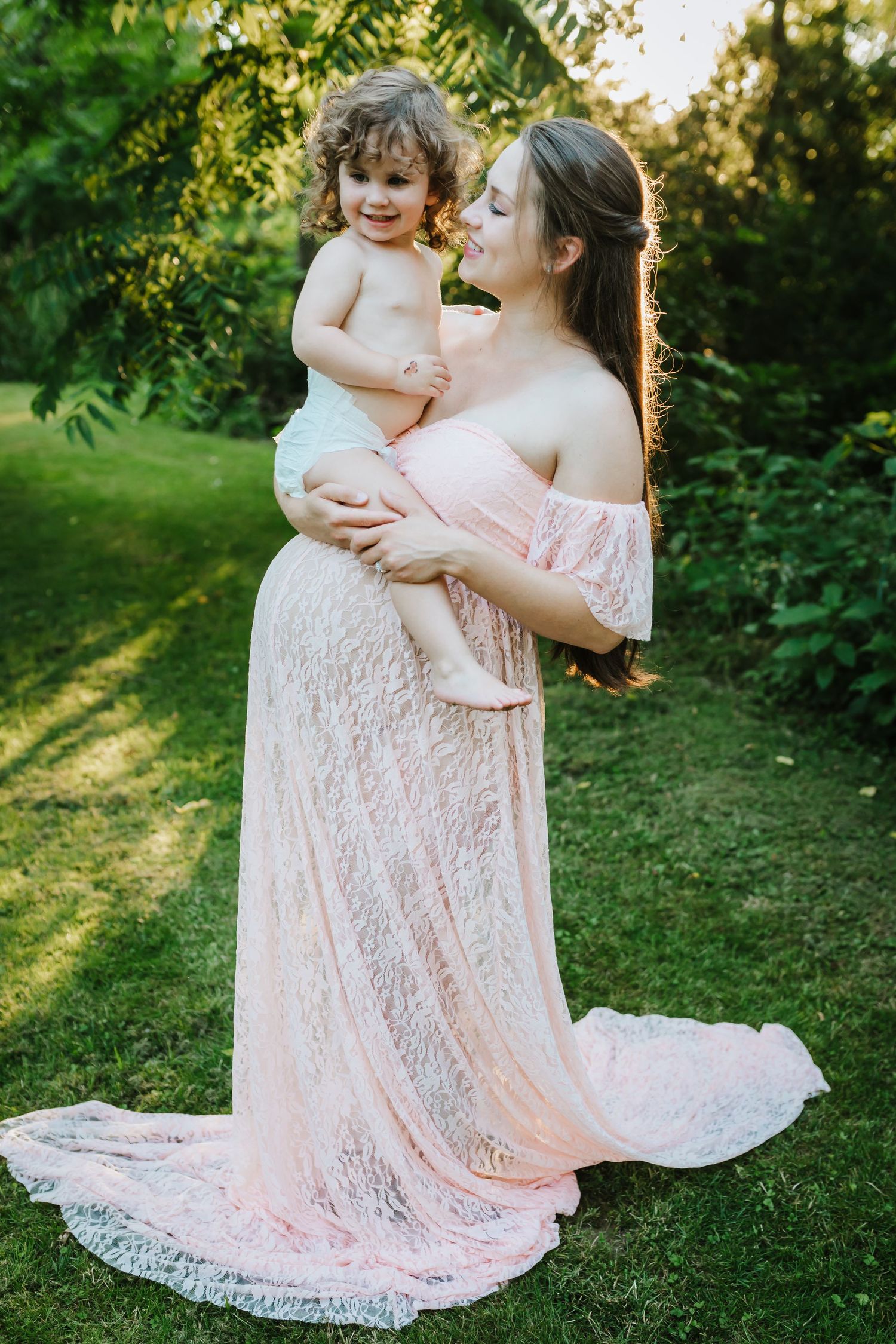 Pregnant mom holding her little girl and smiling at her as she laughs