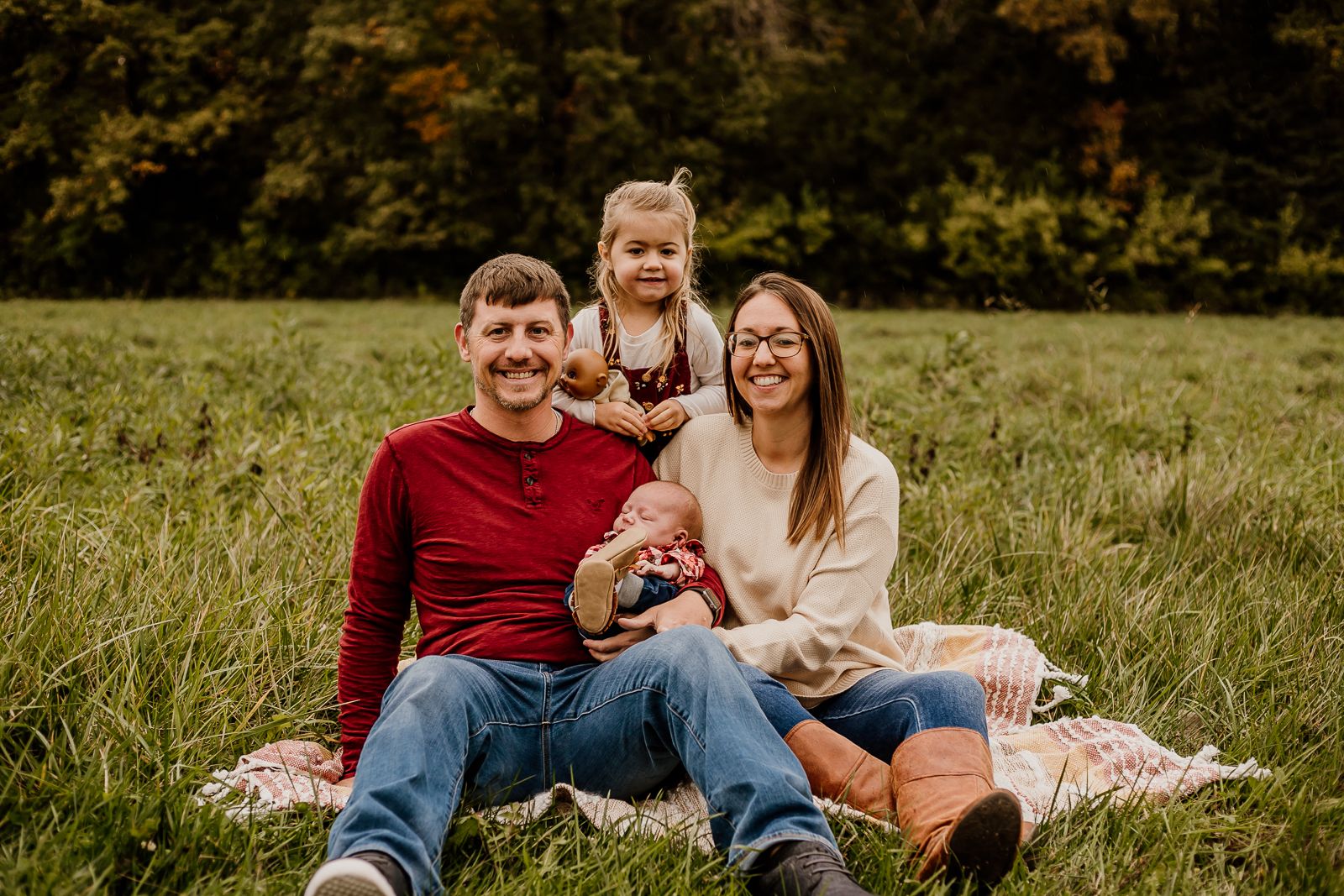 A family sits together on a blanket in a grassy field during golden hour.