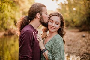 Romantic couple embracing in warm autumn sunlight wearing burgundy and green sweaters.