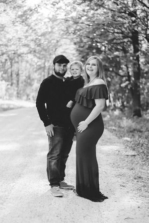 Black and white maternity photo of a couple walking together on a tree-lined path.