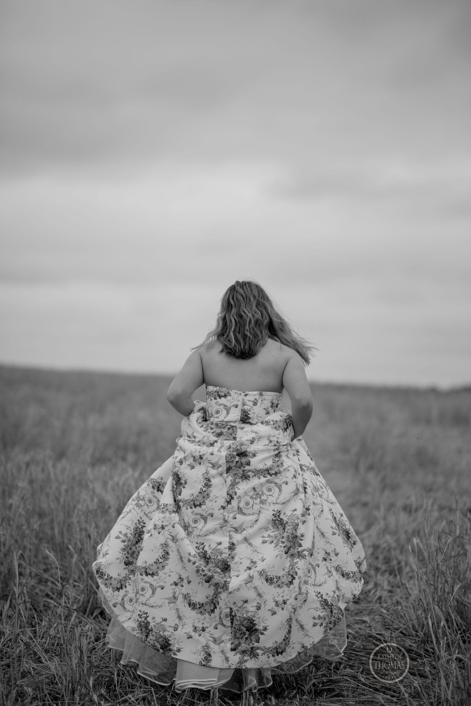 Black and white image showing back view of floral dress in meadow landscape.