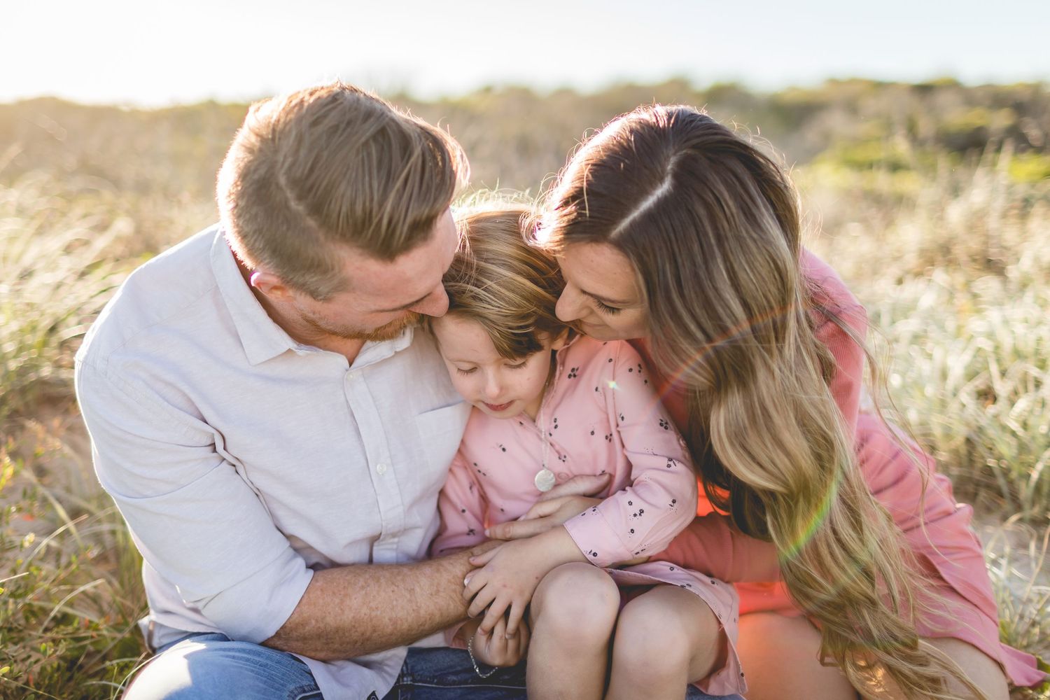A family shares an intimate moment together while sitting in golden sunlit grass.