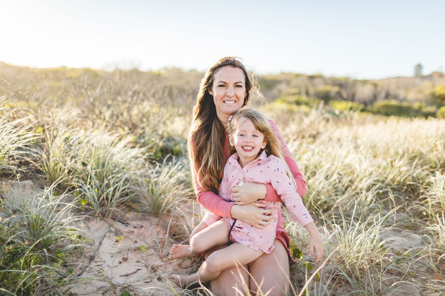 Mother and child sharing a joyful moment while sitting in wild grass at sunset.