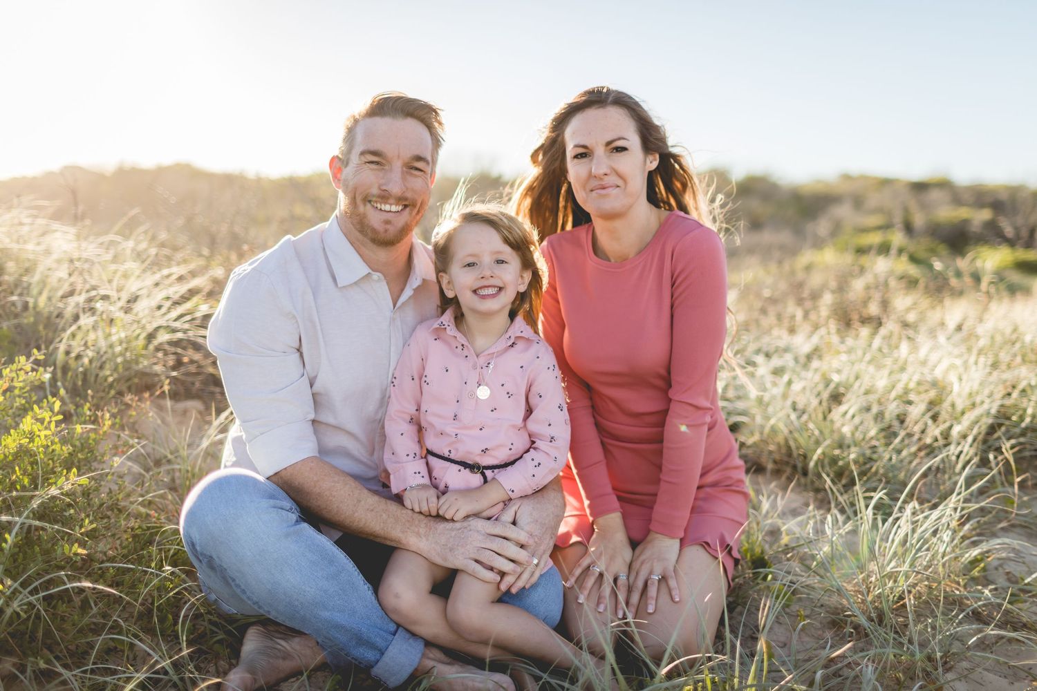 A family sits together on a grassy hillside during golden hour.