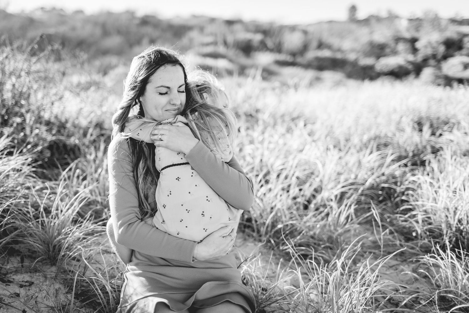 Black and white portrait of loving embrace in natural outdoor setting among tall grass.