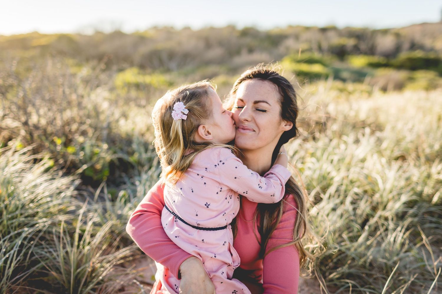 Tender moment shared between parent and child in golden field at sunset.