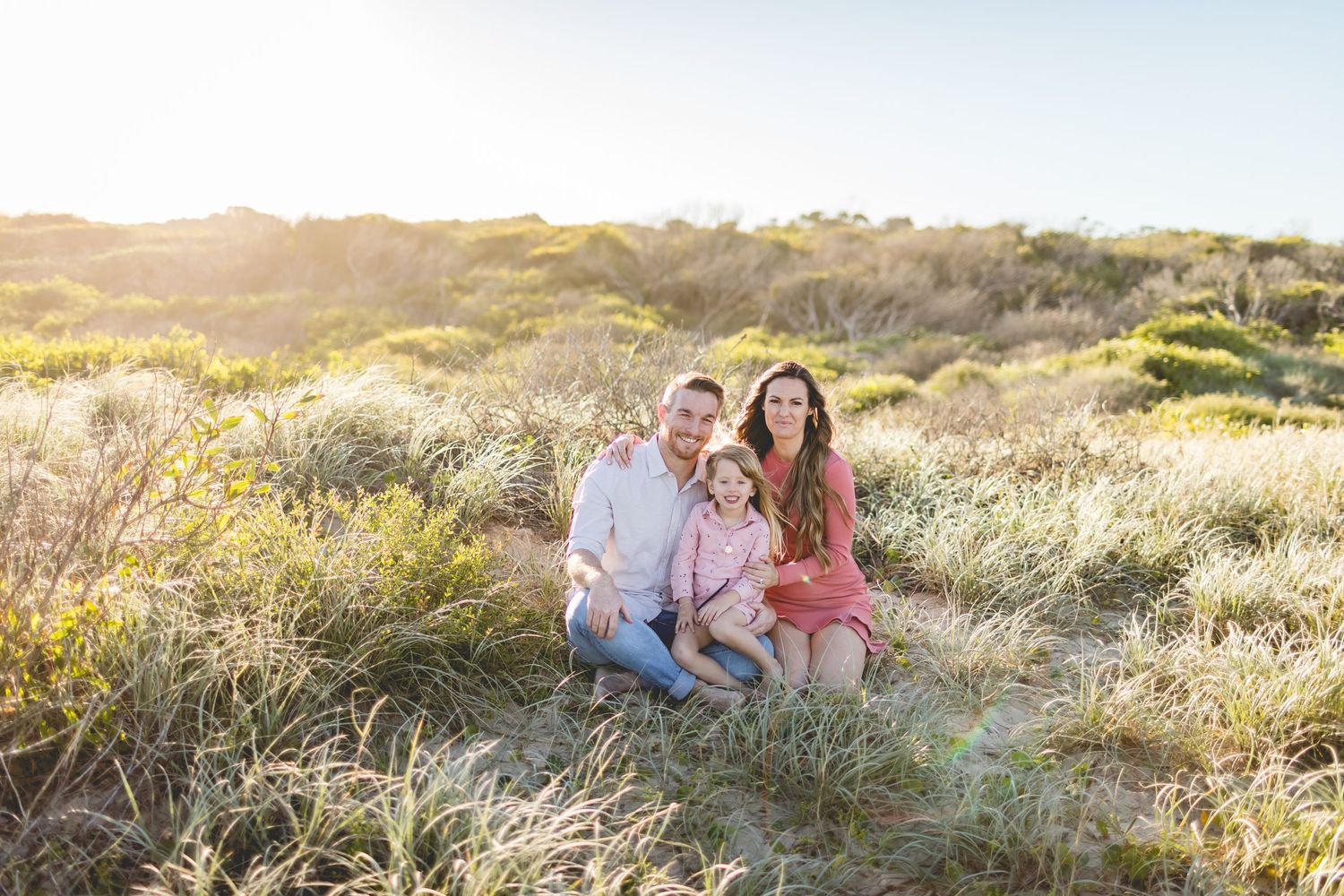 A family shares a tender moment while sitting in tall grass during sunset.