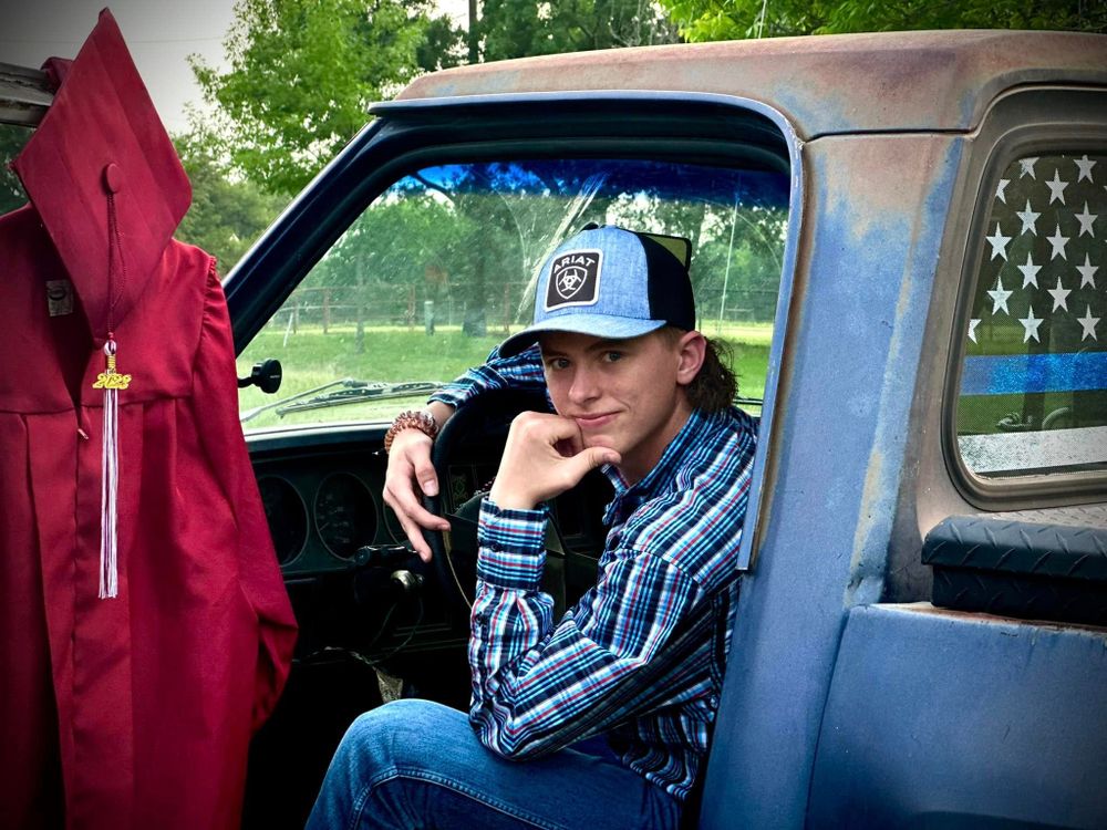 Senior photo showing person in blue plaid shirt and baseball cap sitting in vintage pickup truck.