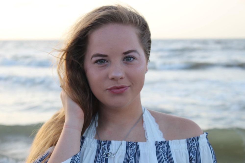 Portrait at sunset featuring off-shoulder striped top against ocean backdrop.