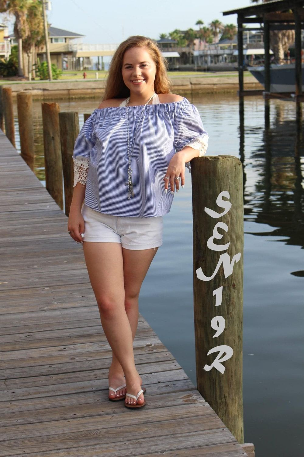 Summer fashion photo on dock with person in off-shoulder white top and shorts next to marina post.