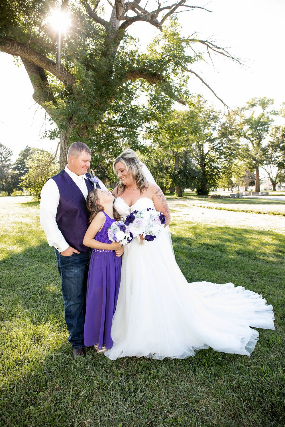 A wedding portrait featuring purple accents and a flowing white dress under a majestic tree.