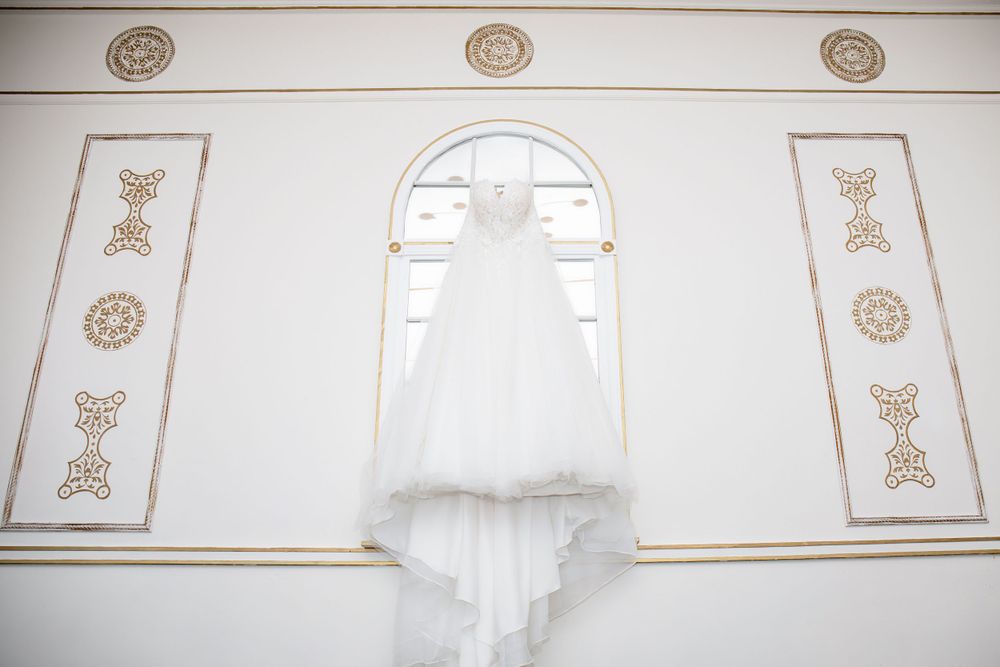 White wedding dress hangs elegantly against an ornate wall with decorative architectural details.