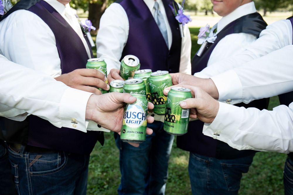 Group toasting with green beer bottles in casual wedding attire.