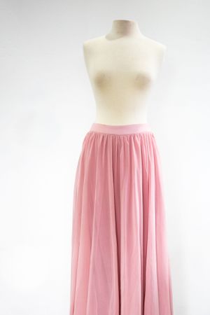 A flowing pink chiffon maxi skirt displayed on an ivory clothing mannequin against white.
