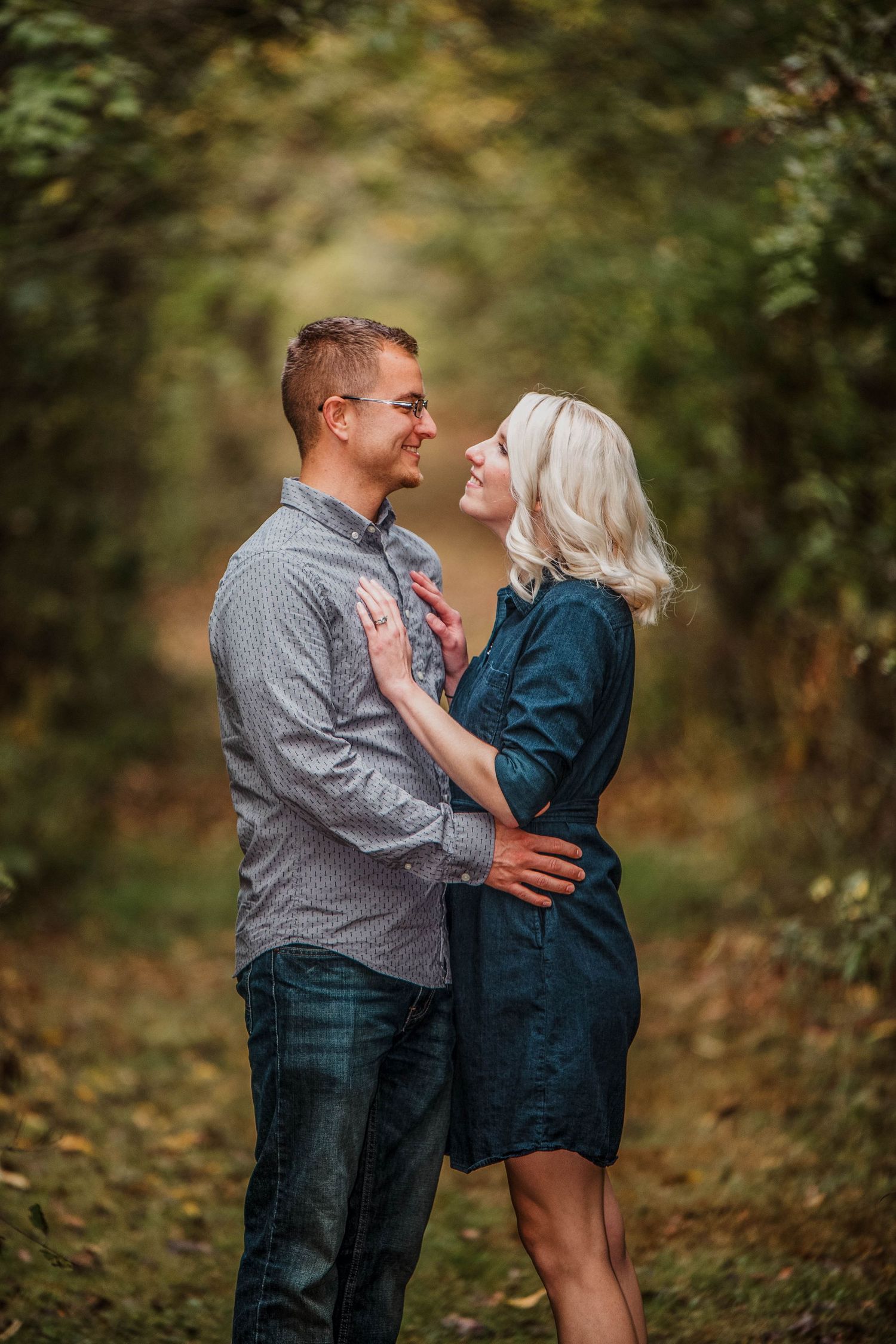 A couple shares an intimate moment on a tree-lined path during autumn.