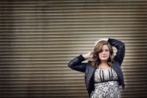 senior pictures in a floral dress and black leather jacket poses confidently against an industrial metal wall background. Duluth