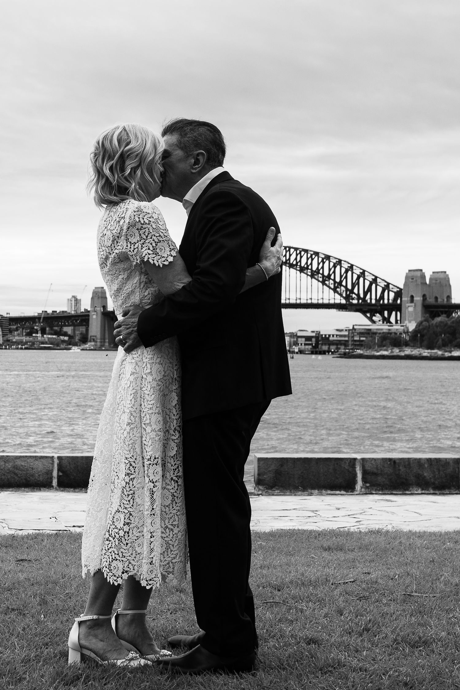 Romantic moment near Sydney Harbour Bridge with a lace dress and formal attire.