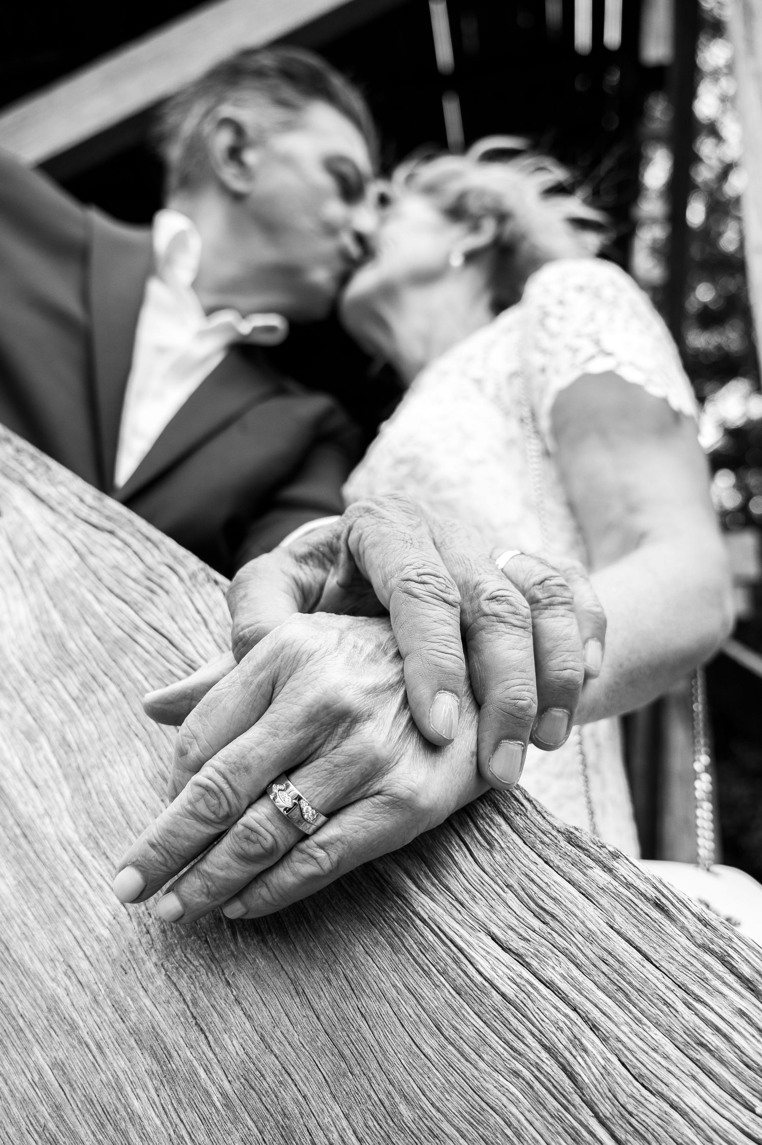 Close-up of hands with wedding ring resting on weathered wood surface.