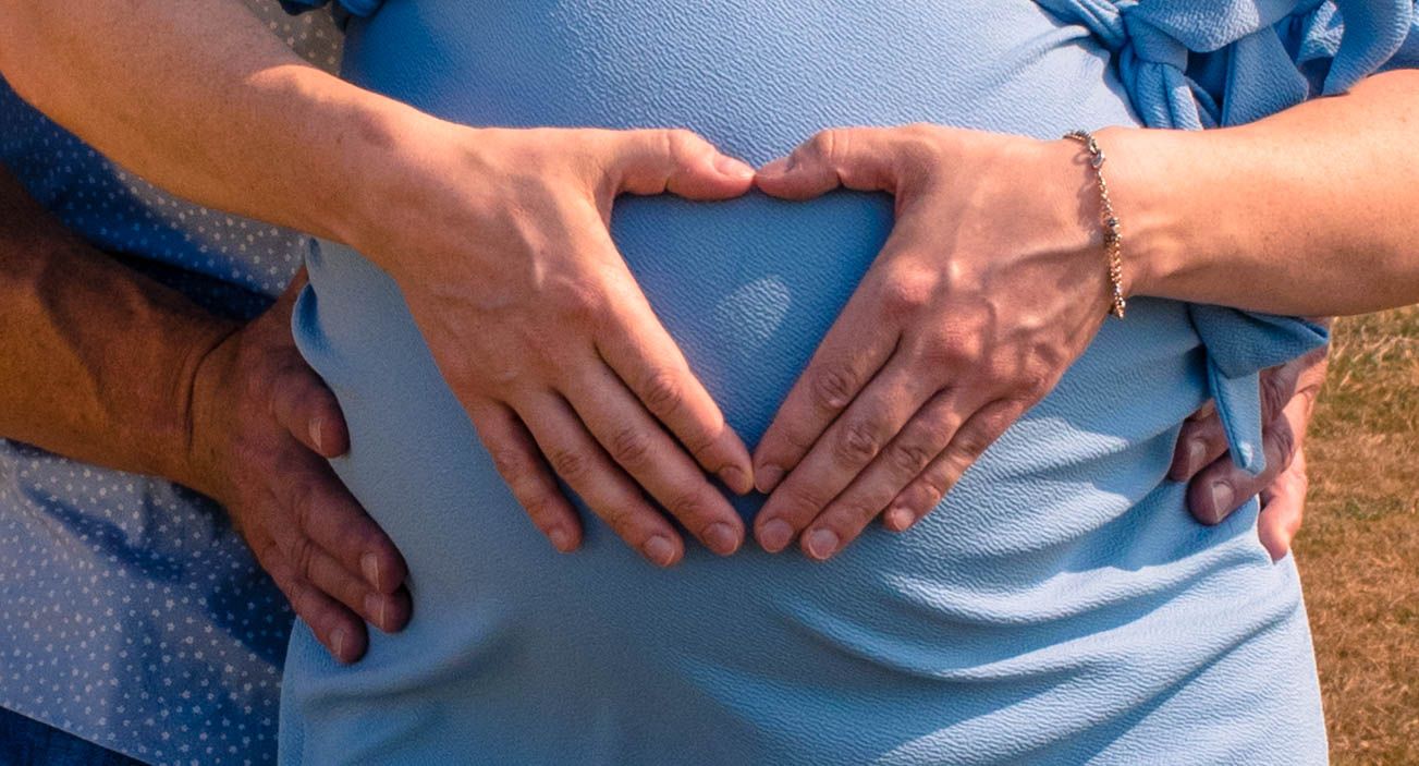 Hands forming a heart shape over a pregnant belly.