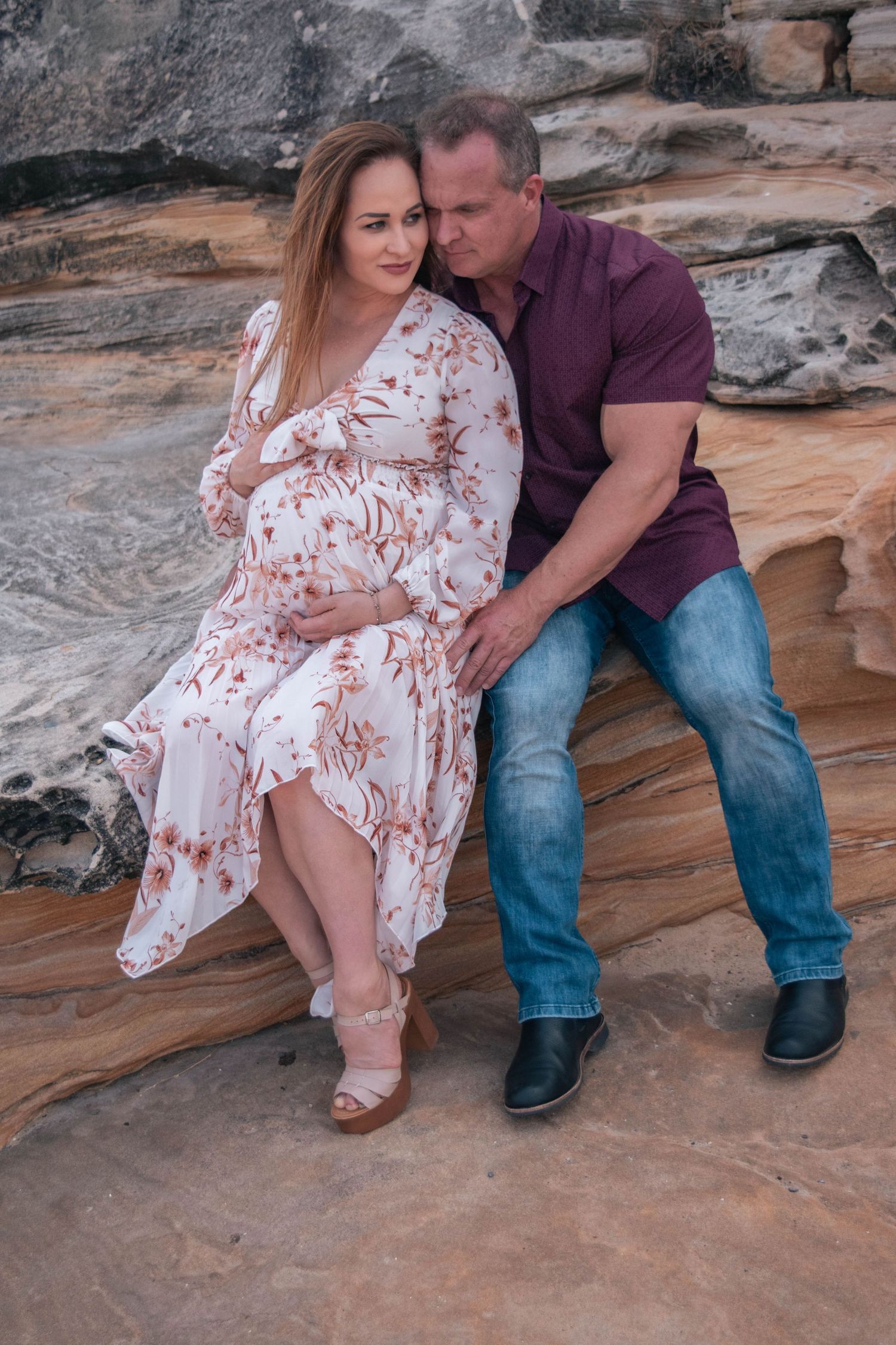 Romantic maternity photo of a couple sitting on red rock formations.