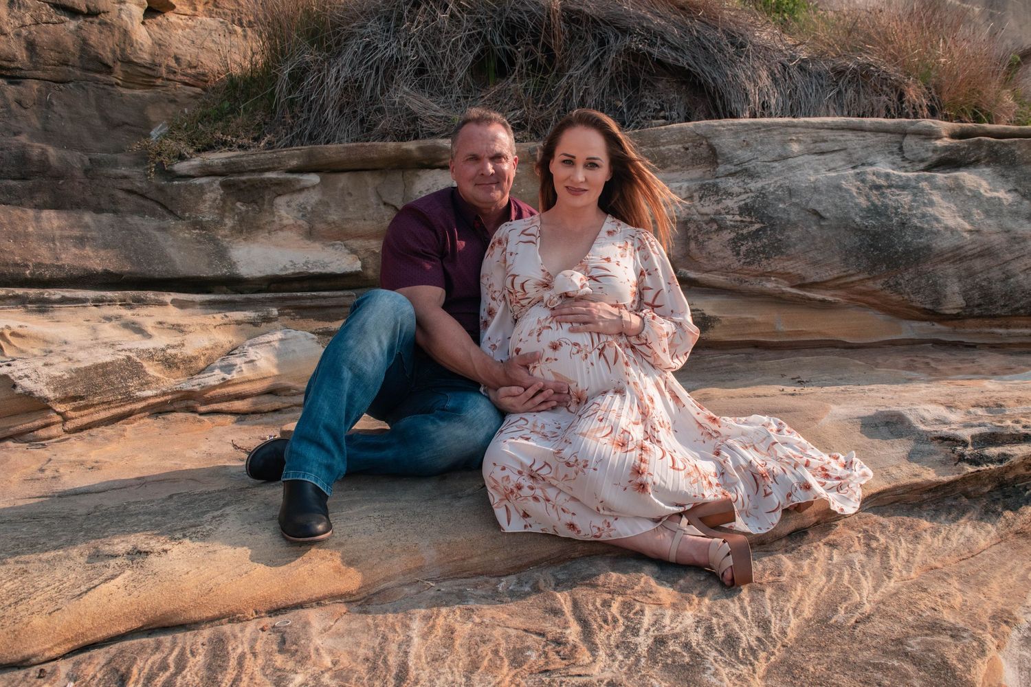 Expecting couple pose together on scenic rock formations during golden hour photo session.